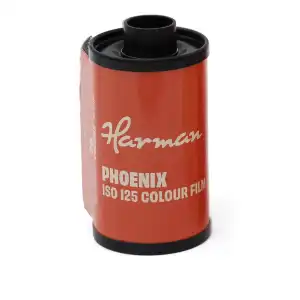 Metalowa rolka filmu fotograficznego typu 135 (35mm) HARMAN Phoenix 125. Kasetka oklejona jest ciemną etykietą z fioletowymi i pomarańczowymi elementami graficznymi oraz wyraźnym logo Phoenix.